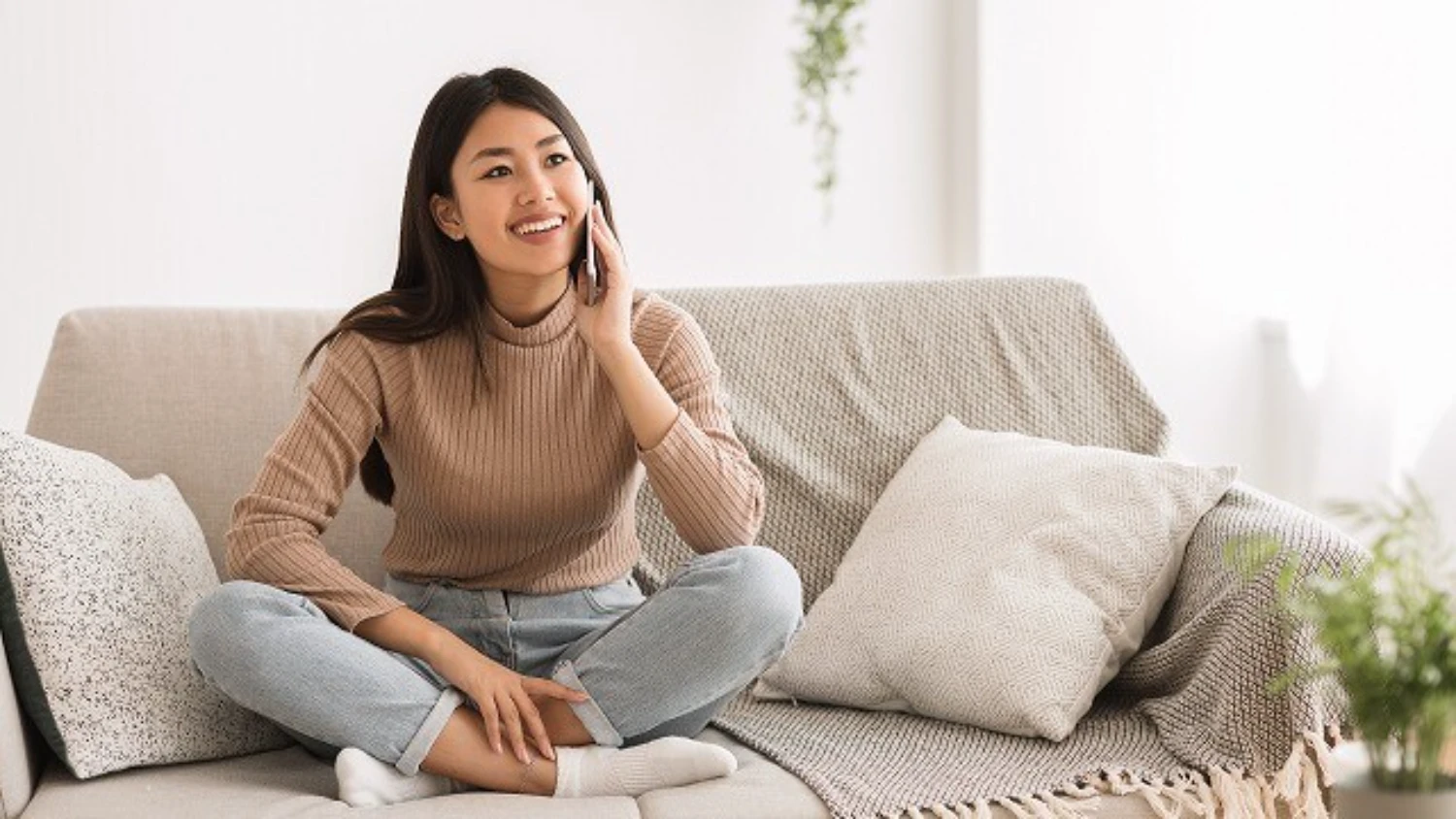 ソファに腰かけ、笑顔で電話する女性